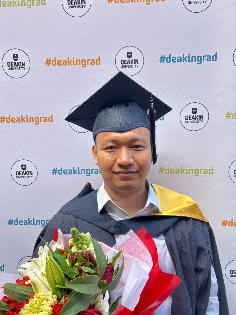Seakleng Ren wearing graduation regalia and holding a bouquet at Deakin University.